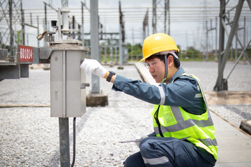 High voltage engineer is working carefully at substation wearing safety gear and yellow helmet, ensuring electrical equipment operates safely and efficiently