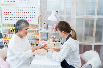 Manicure spa session with senior asian woman and young professional nail technician promoting beauty personal grooming wellness hygiene lifestyle relaxation friendly small salon business environment