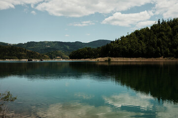 Clear reflection of mountains and sky on the calm surface of Zaovine Lake in summer time Serbia, Tara National Park.