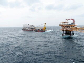 Offshore Platform Operation A large vessel approaches a towering offshore oil platform amidst a choppy sea under a cloudy sky. The scene depicts industrial activity at sea.