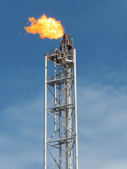 Industrial Flare Stack Against a Clear Blue Sky, Burning Brightly with a Large Flame, Illustrating Energy Production and Combustion Processes.