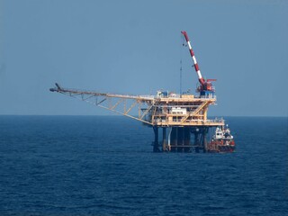 Offshore oil platform stands tall against a vast, deep blue ocean under a clear sky. A support vessel is nearby, ensuring safe operations in the maritime environment.