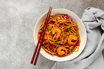 udon stir-fry shrimp noodles with red bell pepper and green onion, served in a black bowl, with chopsticks, gray background,