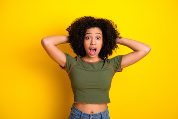 Surprised young woman with curly hair making a shocked expression against a bright yellow background