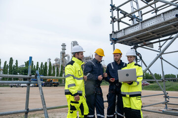 Workers discuss safety measures at a construction site while reviewing plans on a laptop