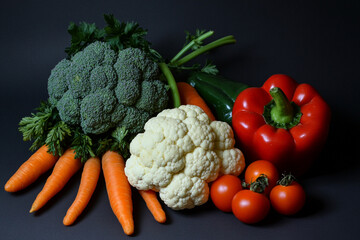 Fresh organic vegetables arrangement: peppers, carrots, tomatoes, broccoli and cauliflower on dark background