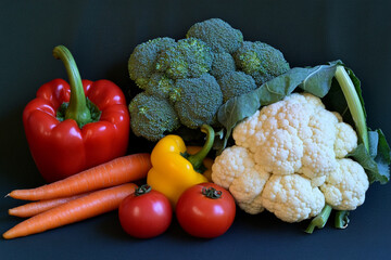 Fresh organic vegetables arrangement: peppers, carrots, tomatoes, broccoli and cauliflower on dark background