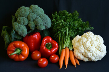 Fresh organic vegetables arrangement: peppers, carrots, tomatoes, broccoli and cauliflower on dark background
