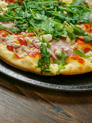 A pizza with ham and spinach on a black tray. The pizza is sitting on a wooden table. Fine Italian cuisine with fresh ingredients ready to be cooked. Fast food meal.