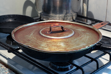 Old frying pan with rusty lid on vintage gas stove closeup