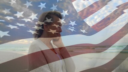 Senior woman standing beach dawn with breeze causing hair tuck, reflecting flag overlay for health - Powered by Adobe