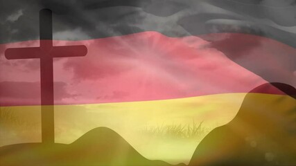 German flag catching breeze over grassy hills by cross showing billowing folds to evoke solemn mood - Powered by Adobe