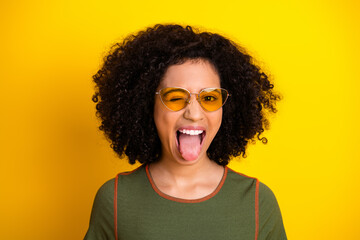 Young woman with trendy style winking and showing tongue on yellow background, expressing playful...