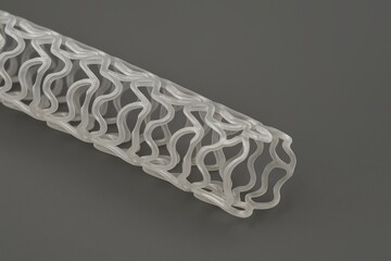 A high-resolution studio photograph of a bioresorbable vascular scaffold made from a translucent polymer, featuring an open-cell, zigzag cylindrical structure. 