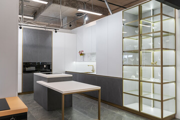 large modern built-in kitchen and kitchen island. kitchen is decorated in white and gray colors. built-in appliances. gold sink and faucet. upper and lower cabinets. illuminated glass display case