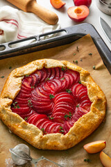 Plum galette with thyme on baking sheet on light background. Healthy homemade fruit pie with plums. Vegan vegetarian cake. Summer concept. Selective focus.