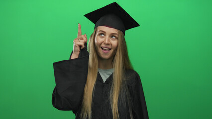 Young caucasian woman in graduation uniform celebrating over isolated green background, pointing...