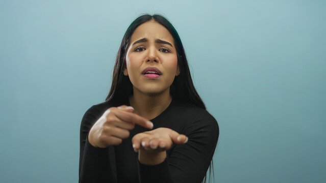 Woman holds her hand in a begging pose with background showcasing a young latin hispanic individual against an isolated blue wall.