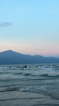 Sunset over sea waves washing the beach sand. Waves sunset mountains sun setting over mountain silhouette. Tropical natural sea view on Molang beach, Indonesia