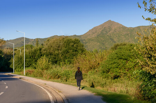 Mujer a lo lejos caminando por el costado de la carretera en una tarde de verano. Cuidado personal. Estilo de vida saludable.
