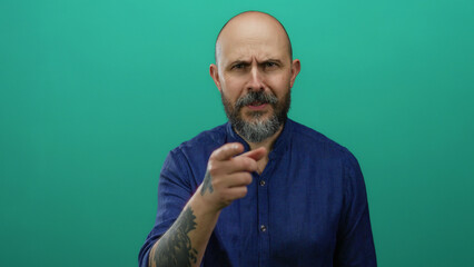 Man pointing with serious expression against green background wearing blue shirt presenting...