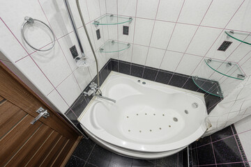 modern bathroom with a white jacuzzi tub, tiled walls and floor, glass shelves, and a wooden door