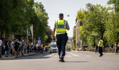 Police officer in reflective vest managing traffic on a sunny urban street with a blurred crowd and vehicles in the background