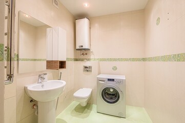 well-lit bathroom with beige tiled walls, green floor, a sink, toilet, washing machine, and a water heater on the wall
