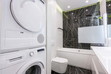 modern bathroom with a washing machine/dryer combo, a toilet, and a bathtub with a black marble...