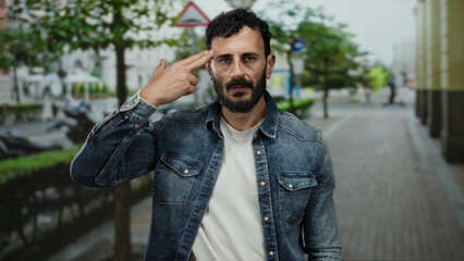 Hispanic man with beard in denim jacket gestures outdoors on a city street, expressing intense...