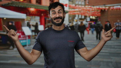 Man with a beard smiling and pointing while standing outdoors on a vibrant city street with...