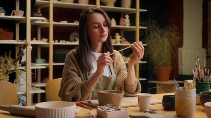 Caucasian woman girl artist designer holding paintbrush pottery tools artisan painter handmade master class in art studio craft painting ceramics female sculptor craftswoman potter choose instrument - Powered by Adobe
