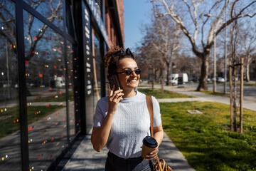 Young interracial happy fashionable woman walking on city street and talking on her cellphone.
