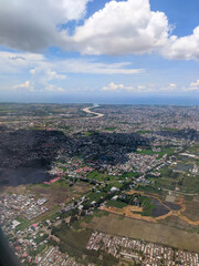 Aerial view of a sprawling city with dense housing, roads, and patches of greenery under a partly cloudy sky, showcasing urban and natural landscapes in harmony.