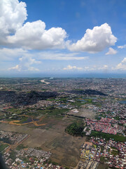 Aerial view of a sprawling city with dense housing, roads, and patches of greenery under a partly cloudy sky, showcasing urban and natural landscapes in harmony.