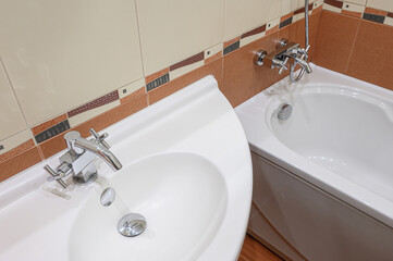 Close-up of a bathroom sink and bathtub, featuring chrome fixtures and beige brown tile accents