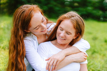 Fototapeta premium Sisters, mother and daughter enjoying a sunny day outdoors in a vibrant green park while sharing laughter and hugs