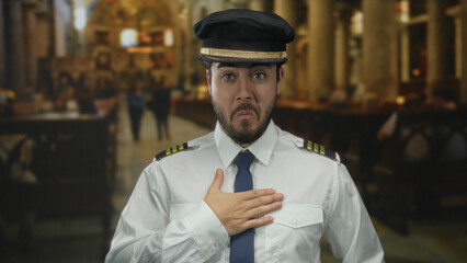Hispanic man with beard in pilot uniform expresses surprise indoors at a church with blurred...