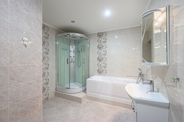 well-lit bathroom featuring a glass-enclosed shower, a white bathtub, a sink, and a mirror. The walls are covered in beige tiles with floral accents