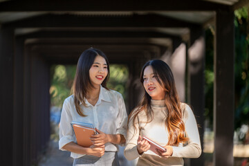 Two women are walking down a hallway, one of them holding a book