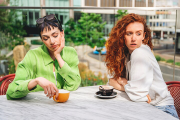 Two women have unpleasant conversation with each other in cafe in  modern urban setting during a sunny day