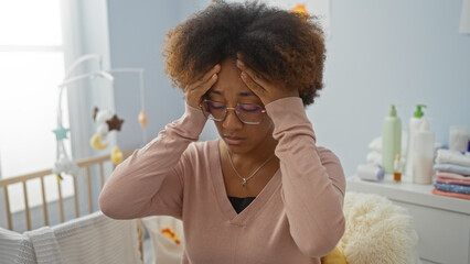Woman holding head in bedroom with baby cradle nearby, expressing stress, conveying motherhood...