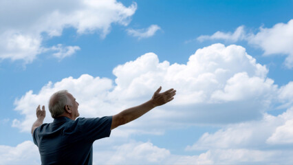 Proud father with arms open to hug gazes at a serene sky with beautiful fluffy clouds in soft light