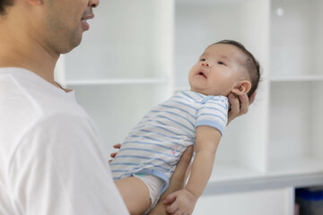A man is holding a baby in his arms. The baby is wearing a blue and white striped shirt. The man is smiling at the baby, and the baby is looking up at him
