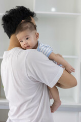 A man is holding a baby in his arms. The baby is wearing a blue and white striped shirt. The man is smiling at the baby, and the baby is looking up at him
