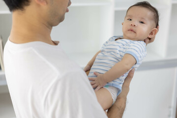 A man is holding a baby in his arms. The baby is wearing a blue and white striped shirt. The man is smiling at the baby, and the baby is looking up at him
