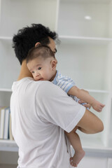 A man is holding a baby in his arms. The baby is wearing a blue and white striped shirt. The man is smiling at the baby, and the baby is looking up at him
