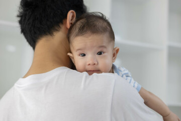 A man is holding a baby in his arms. The baby is wearing a blue and white striped shirt. The man is smiling at the baby, and the baby is looking up at him
