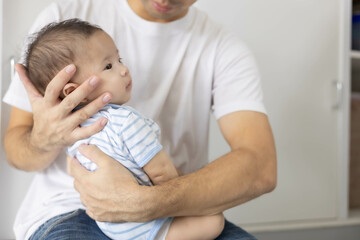 A man is holding a baby in his arms. The baby is wearing a blue and white striped shirt. The man is smiling at the baby, and the baby is looking up at him
