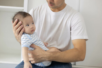 A man is holding a baby in his arms. The baby is wearing a blue and white striped shirt. The man is smiling at the baby, and the baby is looking up at him
